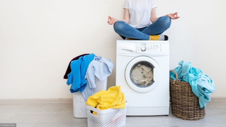Personne assise en tailleur sur un lave-linge entouré de paniers de linge coloré